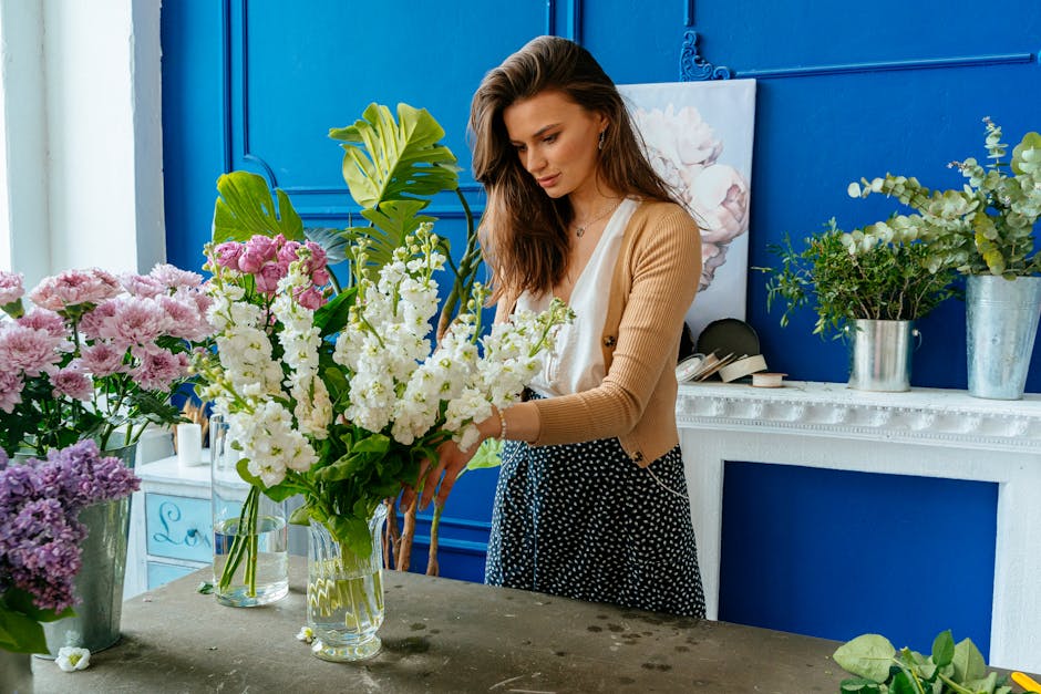 A collection of three floral arrangements on a rustic wooden surface, featuring fresh flowers with predominantly yellow, white, and pink blooms. The arrangement to the right is in a tall, clear glass 