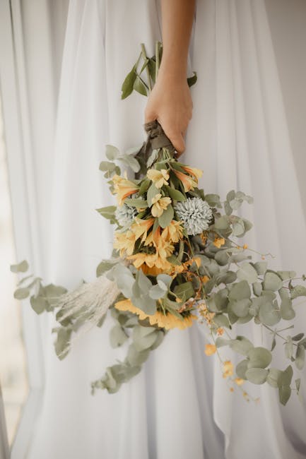 A decorative wedding backdrop featuring a white fabric background with the gold monogram initials 'TL' in the center, surrounded by pastel-colored floral arrangements of cream, blush, and peach roses,